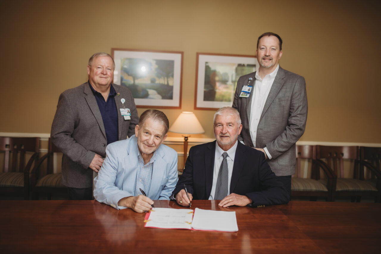 Five healthcare professionals signing a document at a conference table in an office setting.