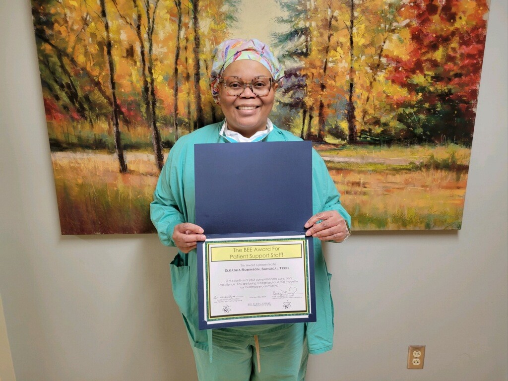 Healthcare staff member holding BEE Award for Patient Support Staff certificate in clinical setting.