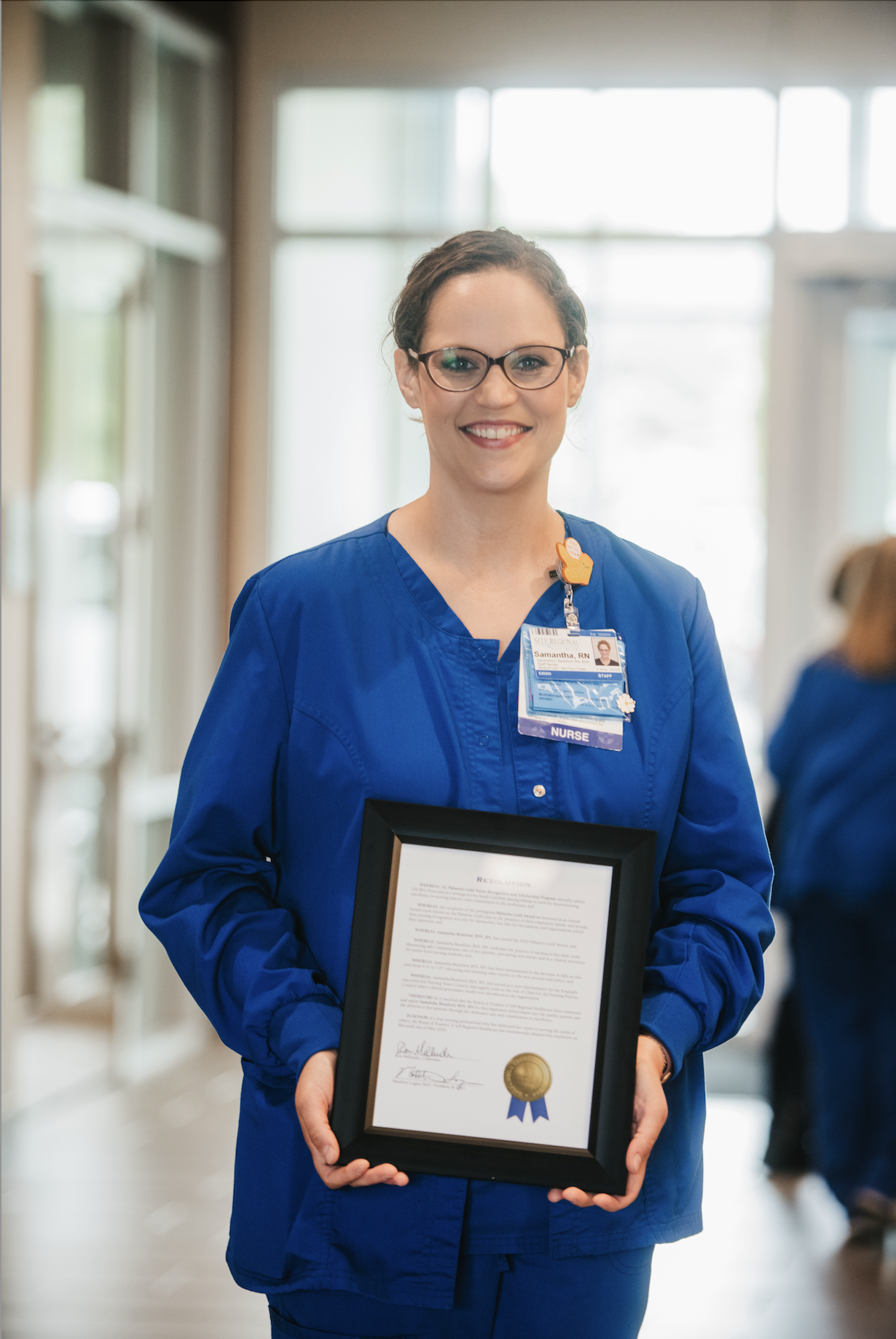 Nurse holding framed award certificate in hospital hallway