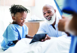 Healthcare provider showing digital tablet to young patient in hospital bed during medical visit.