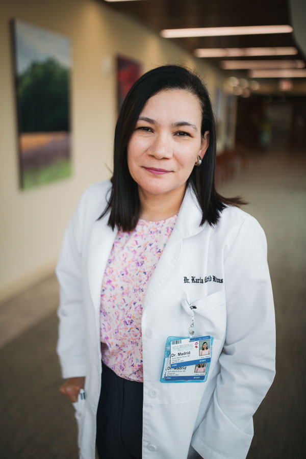 Healthcare professional wearing white coat and ID badge standing in hospital corridor
