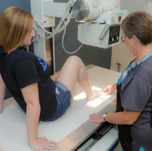 Healthcare provider performing X-ray examination of patient's leg in medical imaging facility.