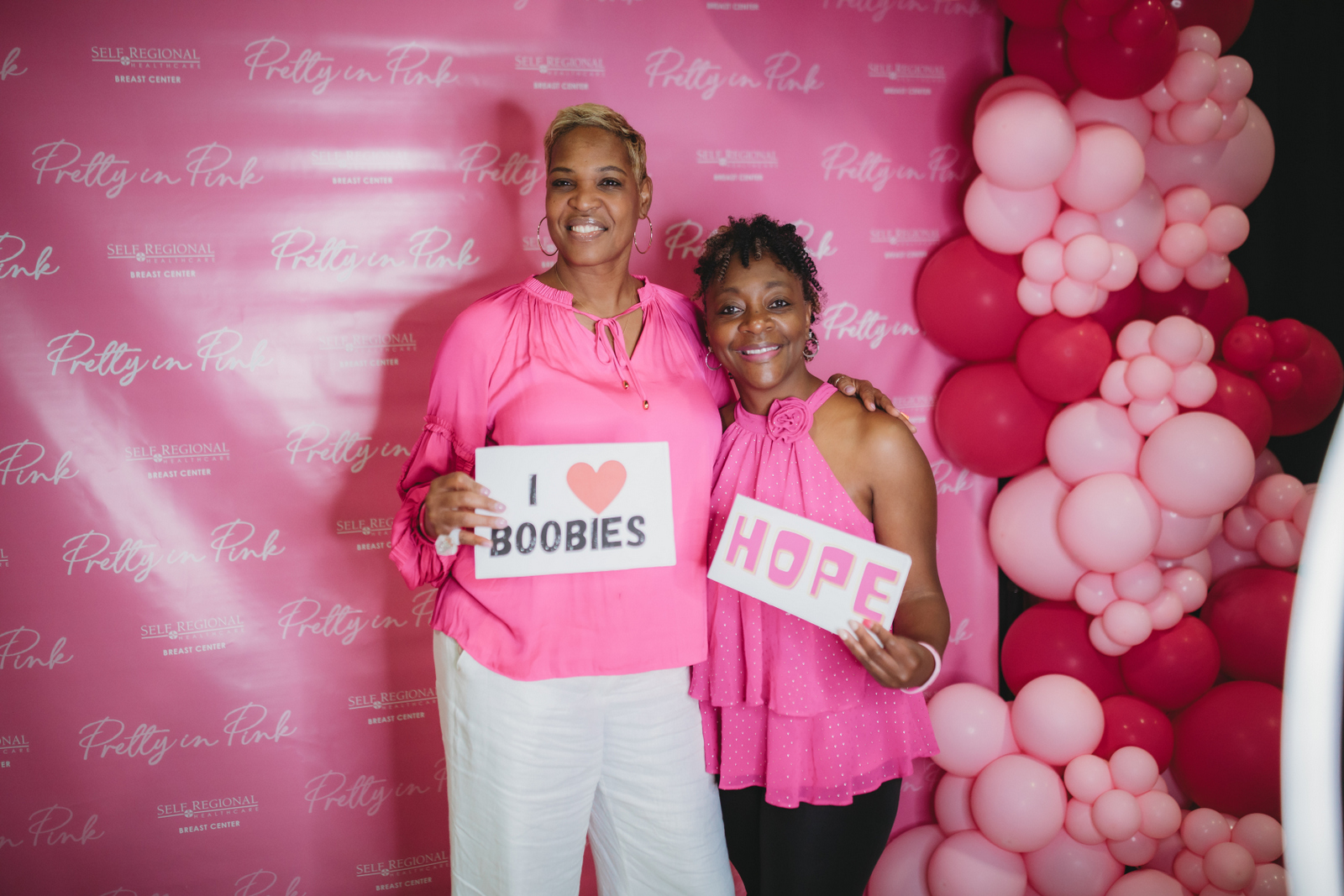 Women at breast cancer awareness event with 'I love boobies' signs