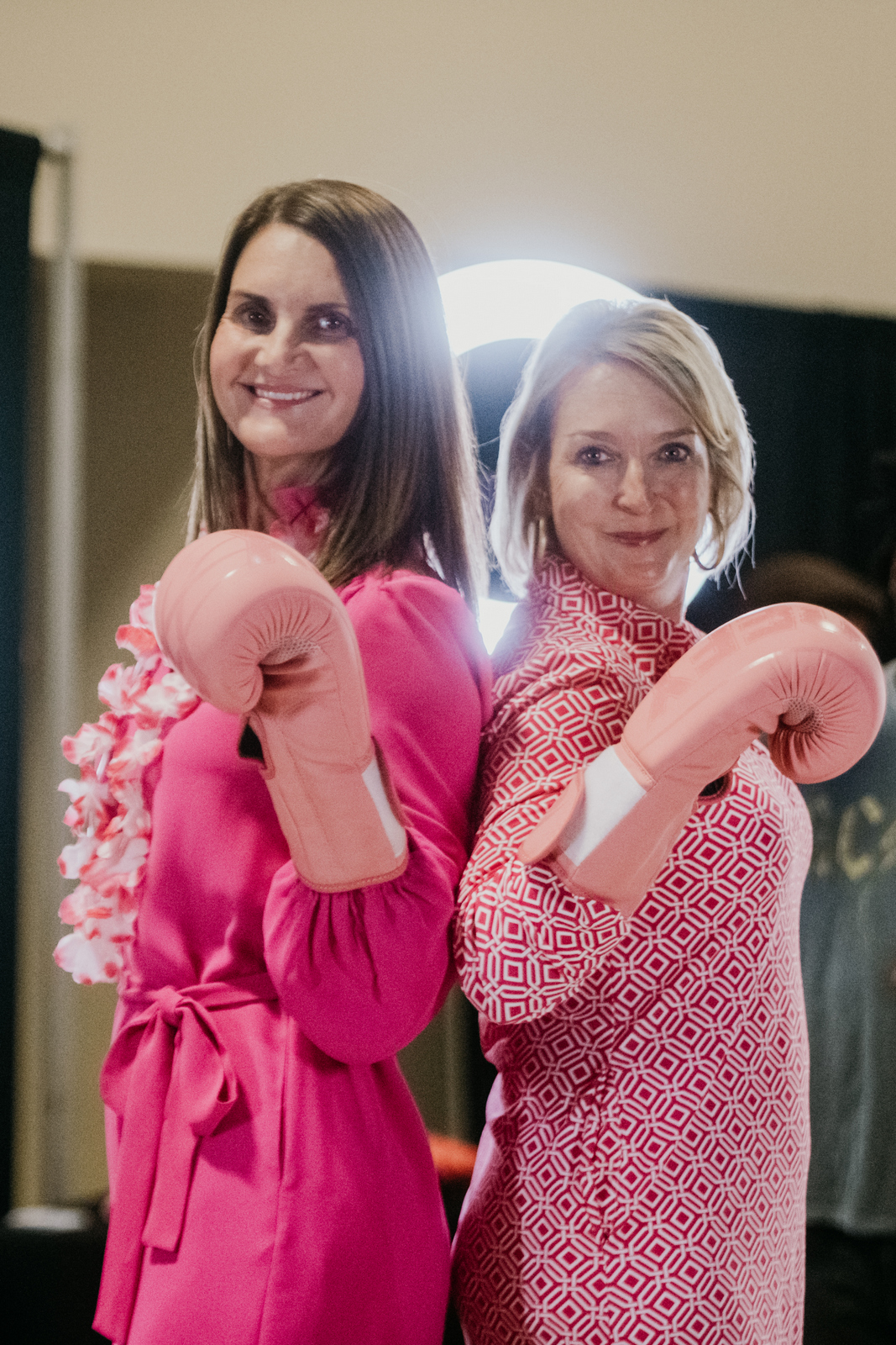 Two women wearing pink boxing gloves smile at a healthcare event promoting fitness and wellness.
