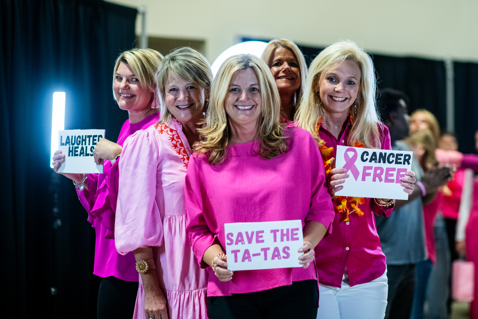 Five women holding signs supporting cancer awareness and prevention at a healthcare event.