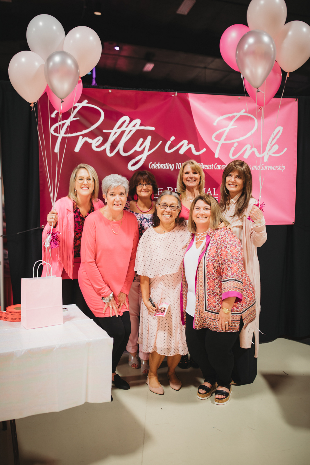 Group of women posing at Pretty in Pink breast cancer awareness event with pink balloons and banner.