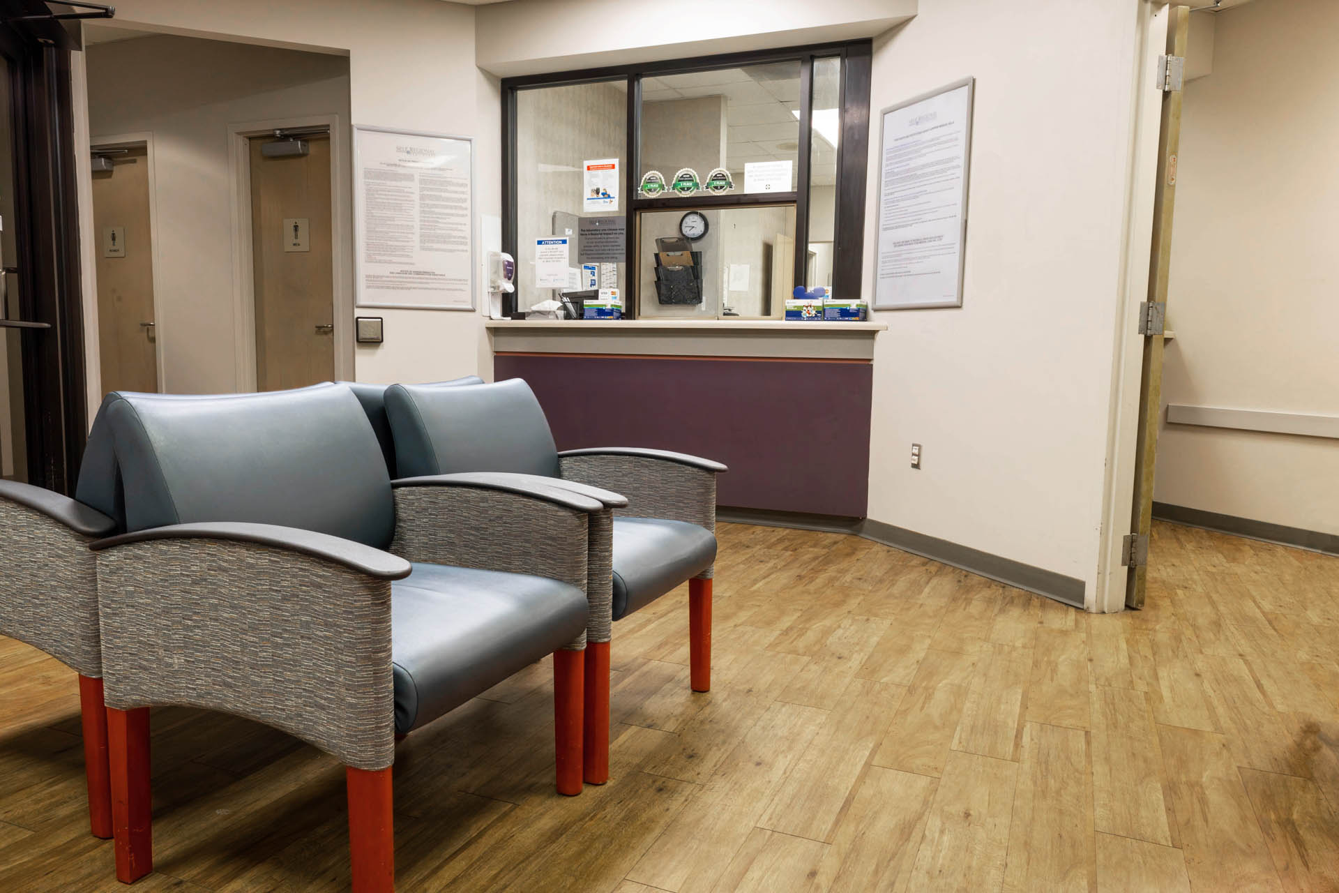 Healthcare waiting room with chairs, reception desk, and informational posters