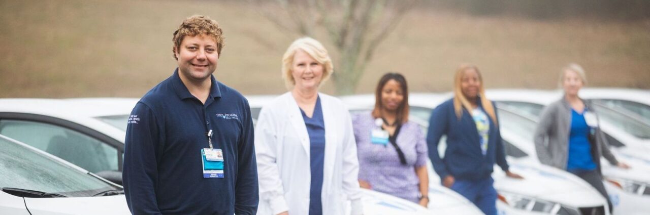 Healthcare team members standing together in a parking lot wearing medical uniforms and badges.