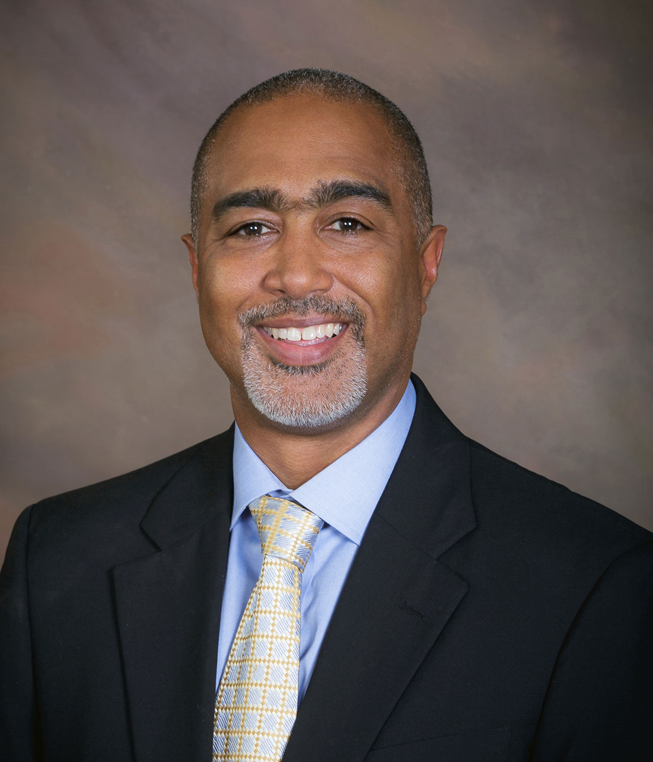 Professional headshot of a healthcare administrator in business attire against a neutral background.