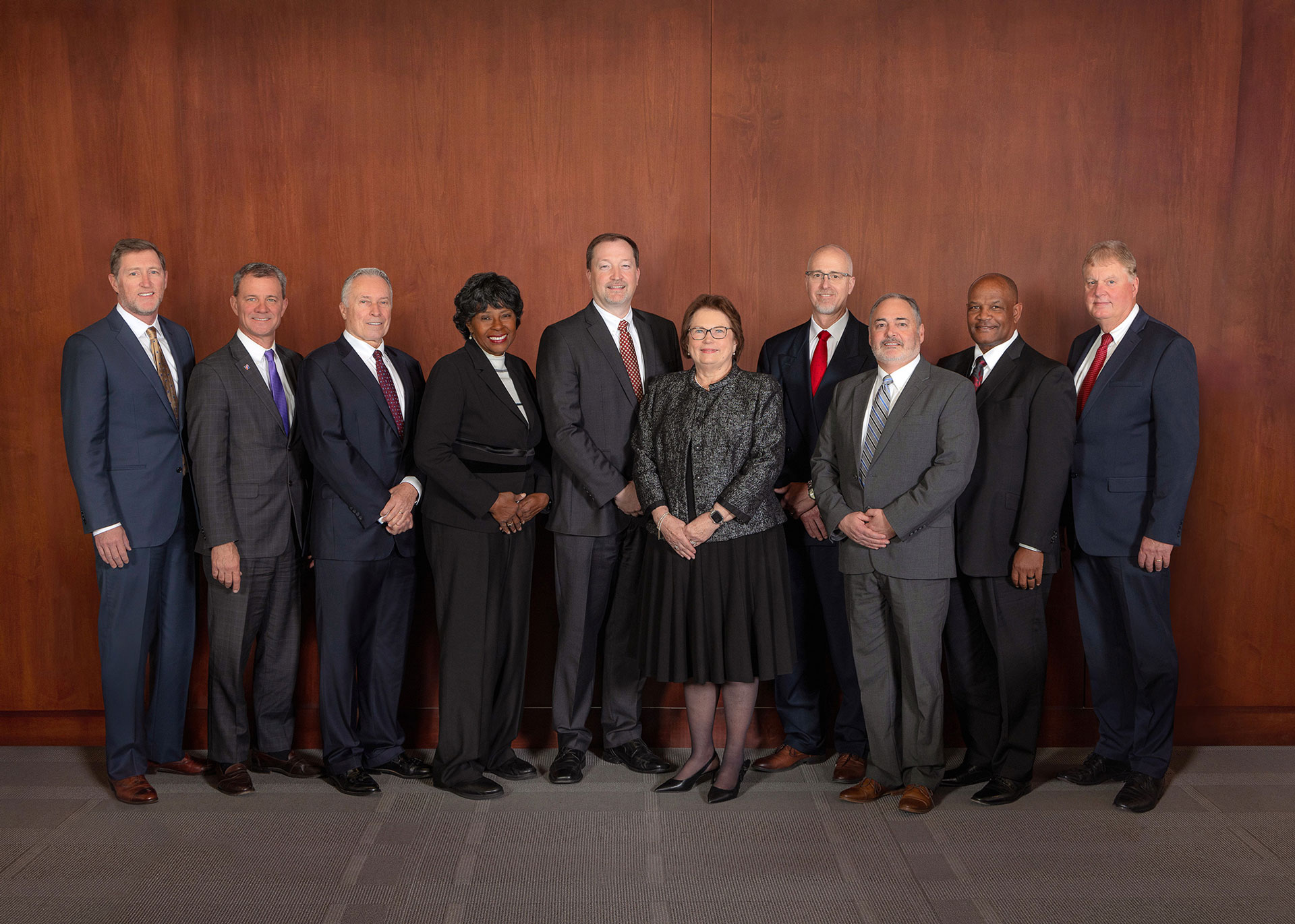 Nine healthcare professionals in business attire standing together for a formal team portrait.