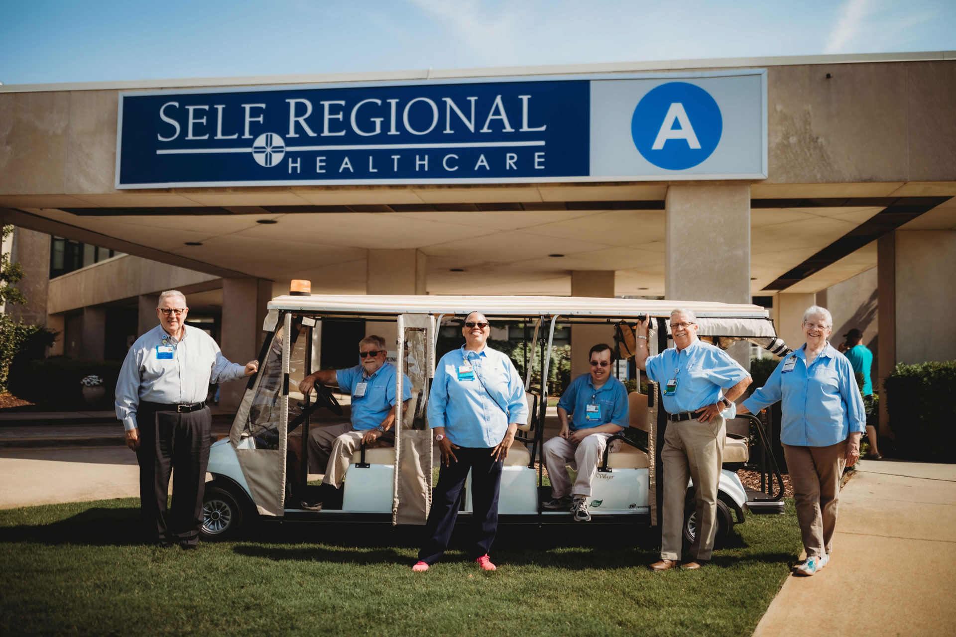 Self Regional Healthcare staff standing with a golf cart in front of the facility entrance.