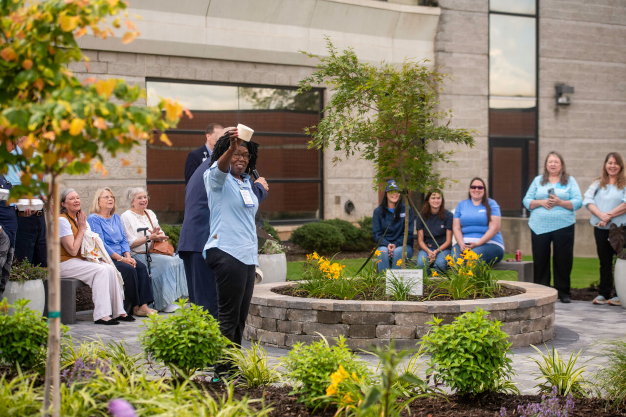 Community gathering in hospital courtyard garden with speaker addressing attendees