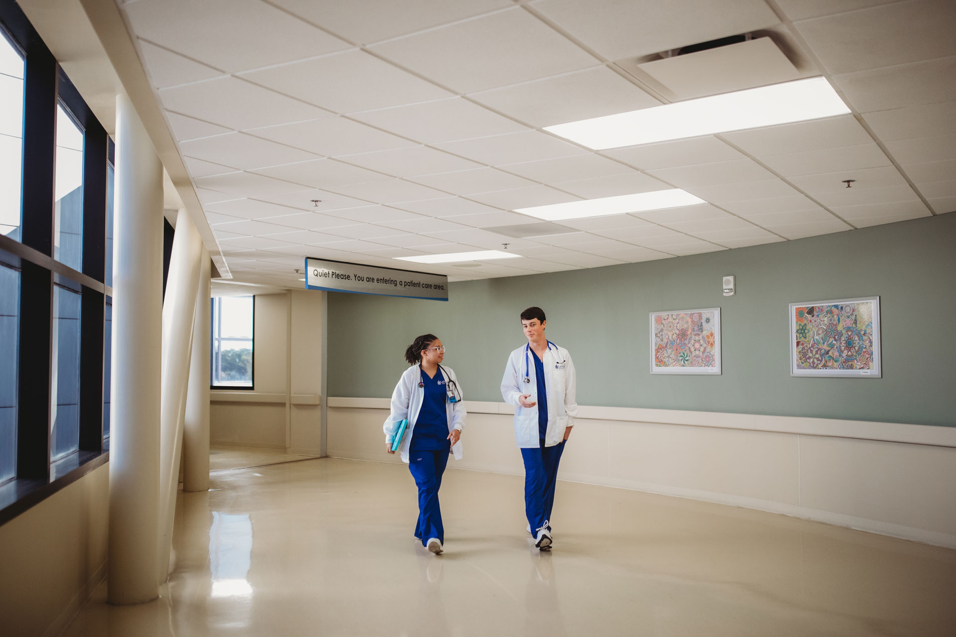 Two healthcare professionals walking and conversing in a hospital corridor.