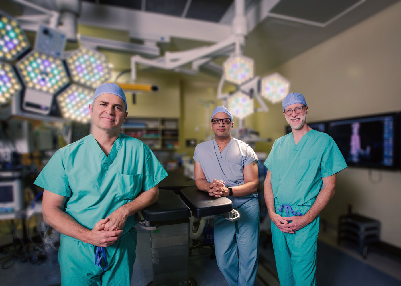Three surgical professionals standing in an operating room beneath overhead surgical lights.